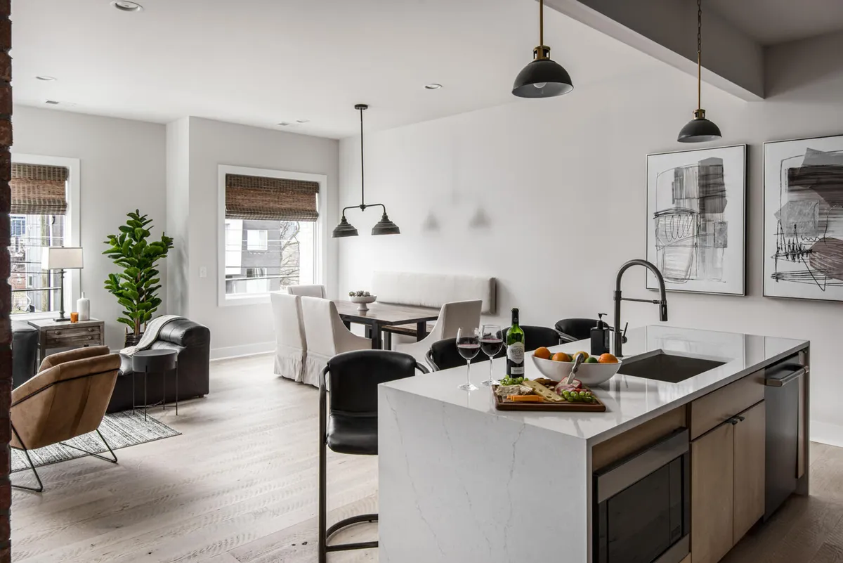 A contemporary, open-concept space featuring a kitchen island, a formal dining table, a living area with comfortable armchairs, and decorative art on the walls. The scene is stylish yet inviting, with elements that encourage both socializing and relaxation.