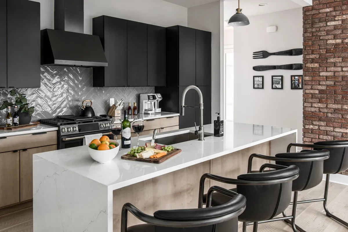 A sophisticated kitchen with a marble island, dramatic black cabinetry, wine glasses, and a wooden cutting board with food. The setting feels both luxurious and cozy, making it ideal for culinary gatherings or intimate celebrations.