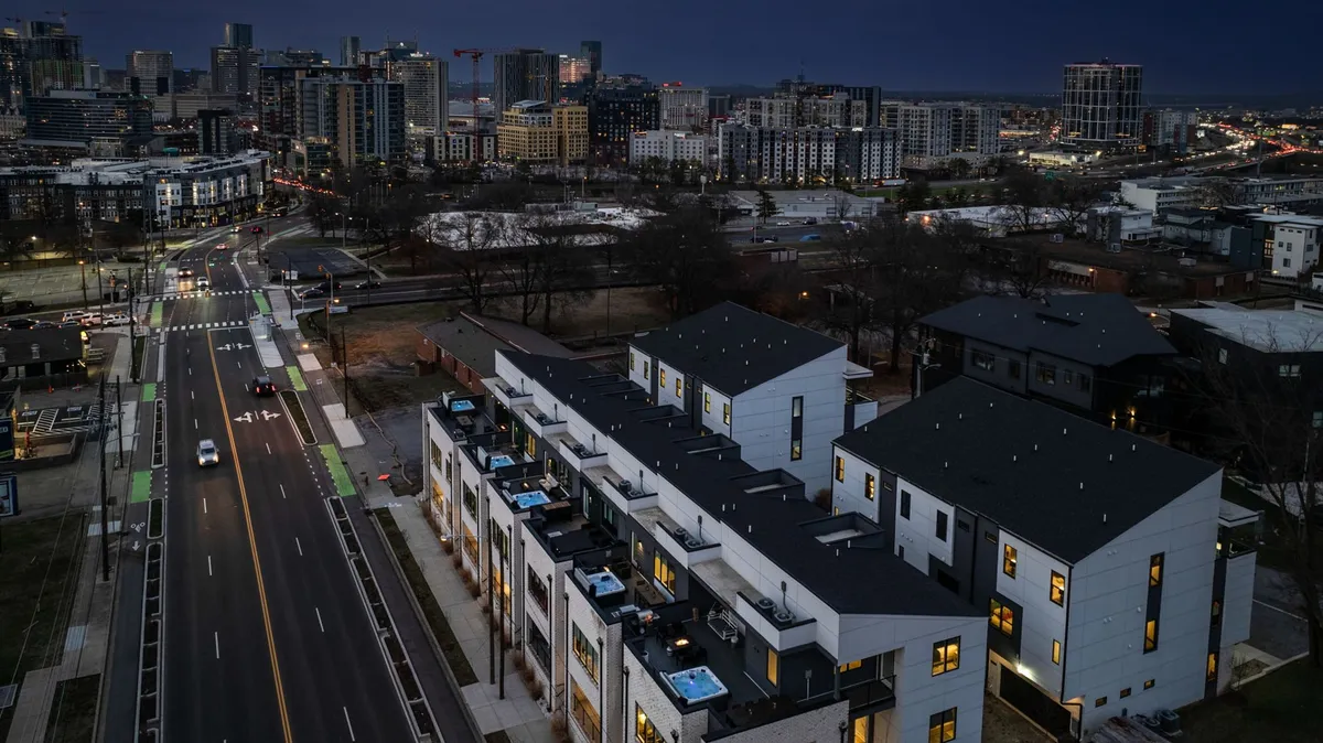 Modern townhouses line the urban street, each with balconies featuring hot tubs and expansive city views. The scene is illuminated by streetlights, and the vibrant skyline creates an energetic, urban backdrop that invites guests to explore and socialize both at home and in the city.