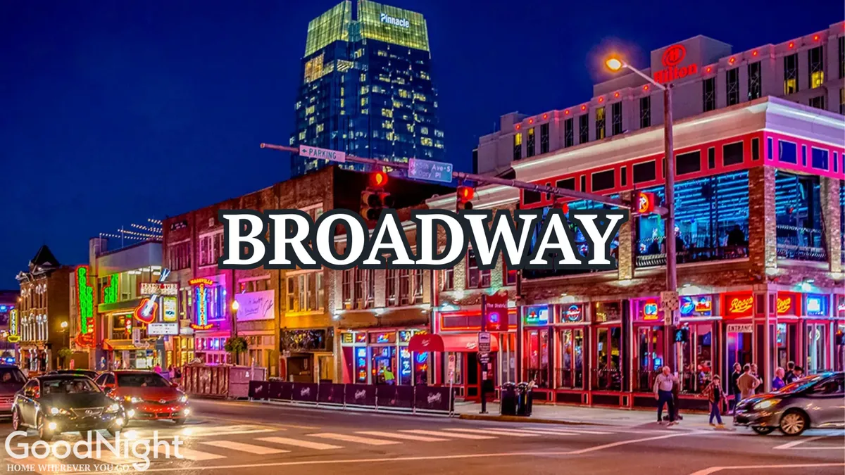 A bustling nighttime city street lined with colorful buildings, glowing neon signs, busy traffic, and crowds enjoying the excitement. The festive lighting and urban vibrancy evoke the energy of Nashville’s nightlife and entertainment options.