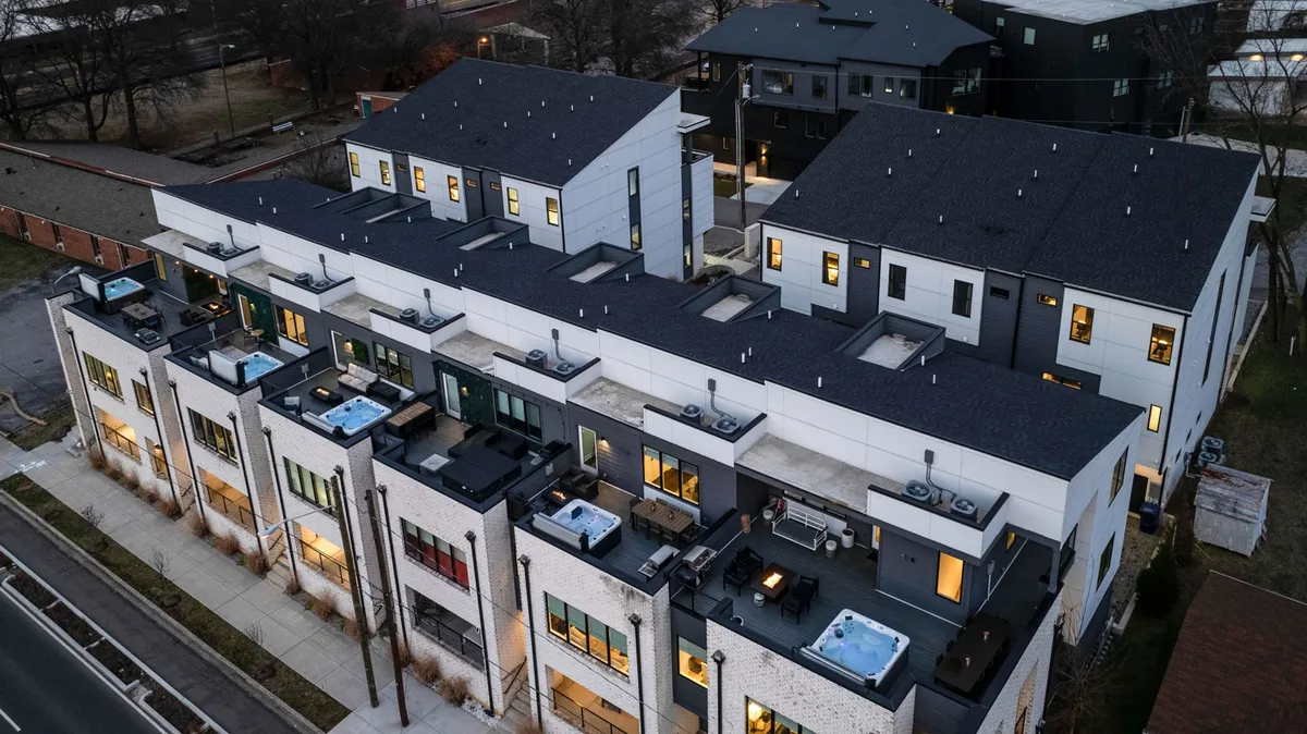 A wide-angle view of the rooftop, illustrating multiple hot tubs surrounded by modern architectural design and ample outdoor seating. The image exudes luxury and social vibrancy, suggesting space for larger gatherings or quieter moments, with the city sprawling in the distance and the evening sky overhead.