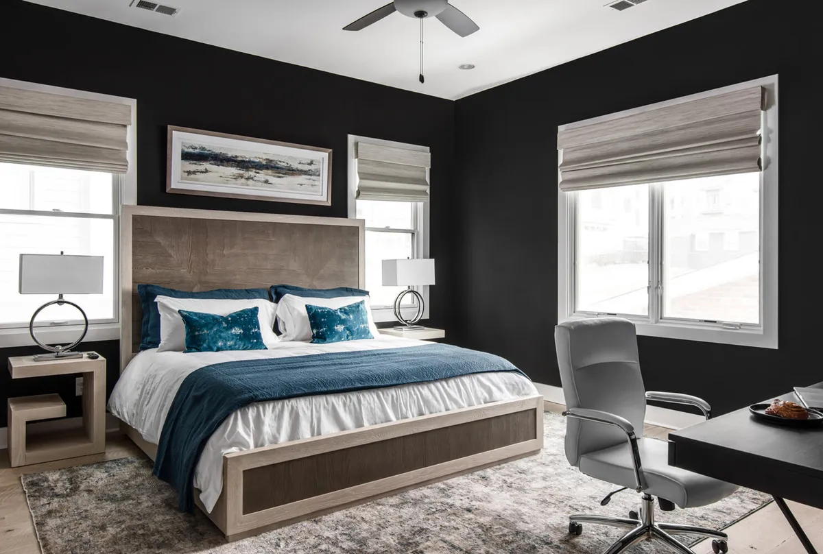 A modern, serene bedroom with blue and white bedding, framed artwork above the bed, and a desk with a chair in the corner—ideal for working or reading in peace.