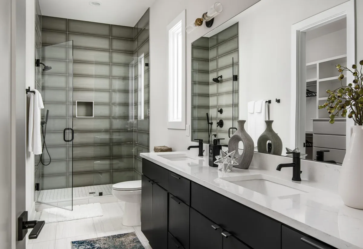 A sophisticated bathroom featuring a dual vanity with black cabinetry, a glass shower enclosure, and large mirrors, evoking a spa-inspired, luxurious feel.