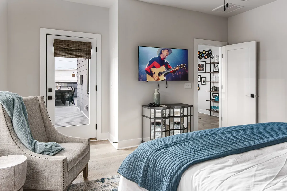 A cozy bedroom scene with a comfortable armchair, television displaying a musician, a bed with textured bedding, and a decorative shelving unit, blending relaxation and creative inspiration.